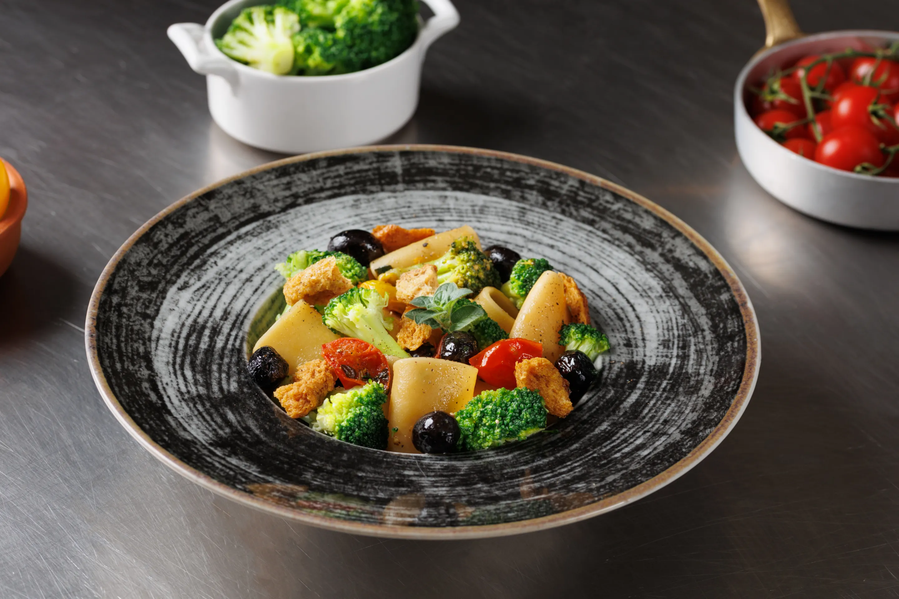 Paccheri con broccoli, pomodorino soleggiato, olive nere fritte, crumble di frisella